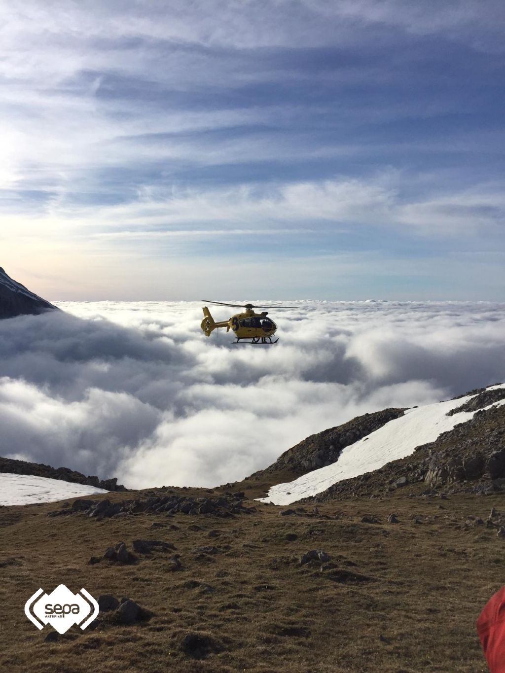 La imagen est tomada desde el lugar donde se encontraban los senderistas. Se puede ver la intensa niebla que estaba por debajo de donde se encontraban. Es el momento  en el que el helicptero evaca al primer grupo, formado por tres excursionitas, hasta