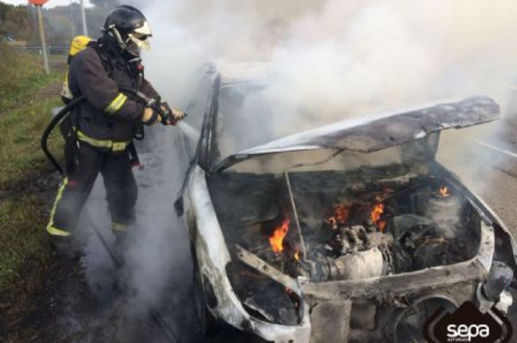 Bomberos sofocando las llamas del coche en Villaviciosa.